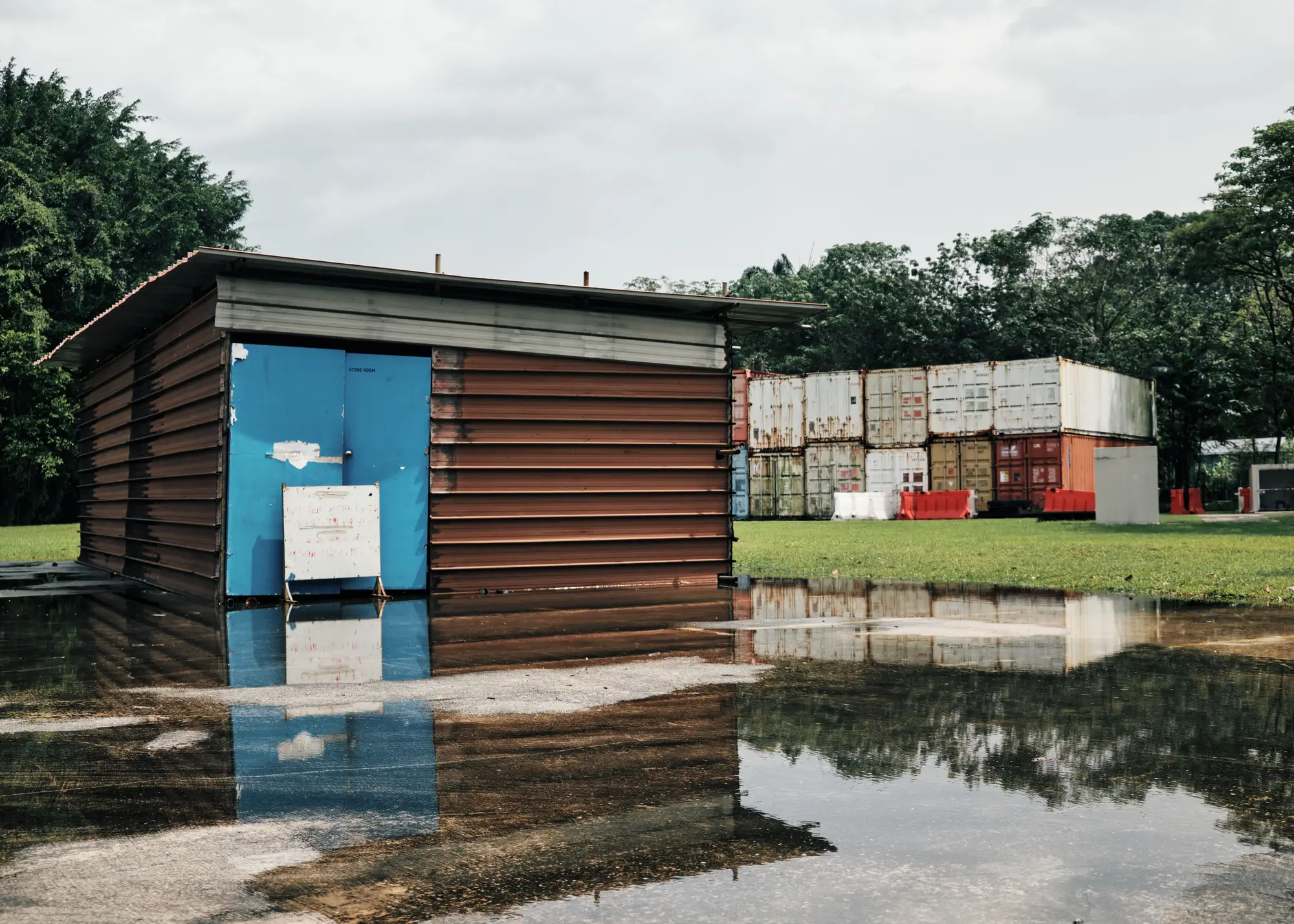 A supplier's storage shed and stacked shipping containers beside standing floodwater